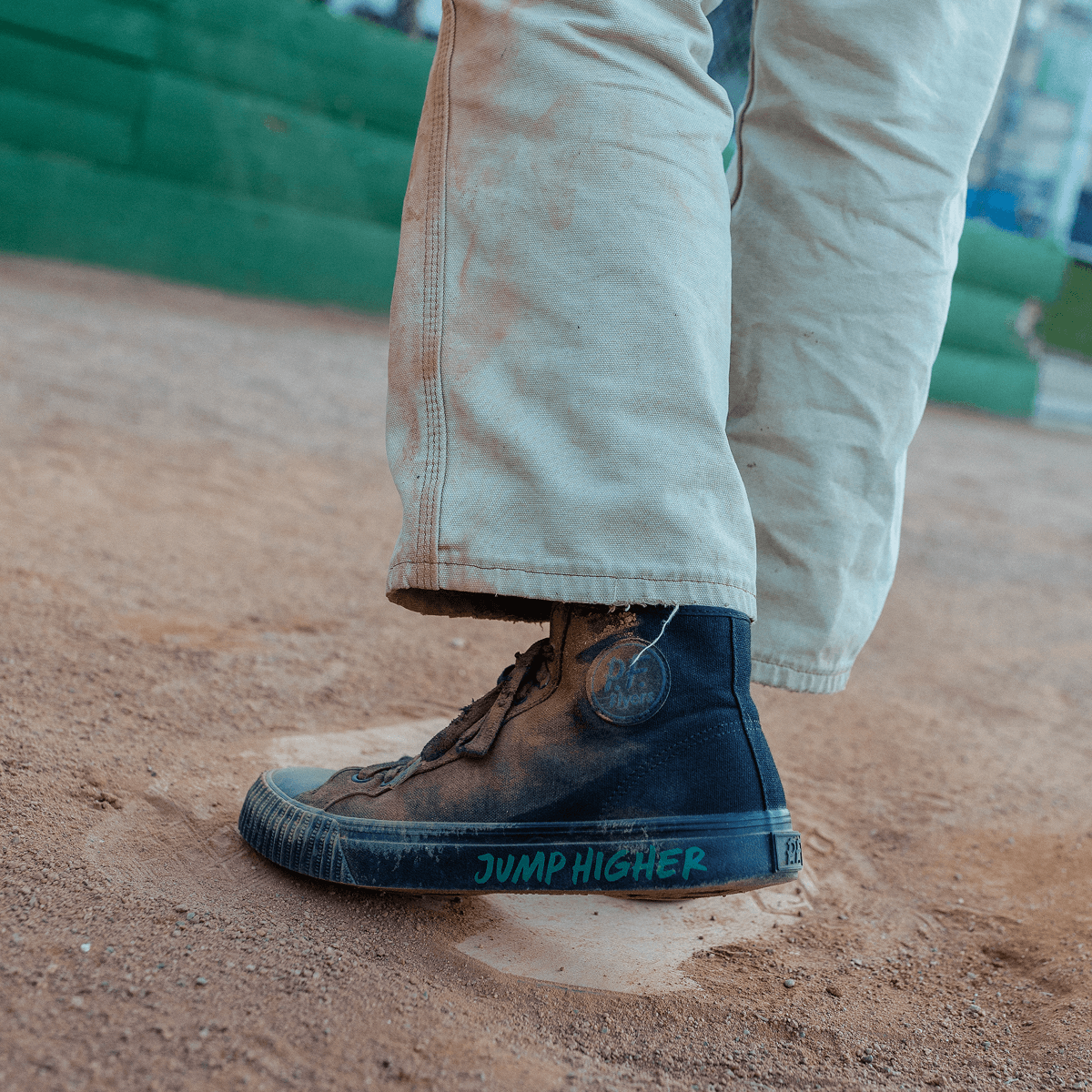 Person wearing a black high-top sneaker with 'Jump Higher' text on a field.