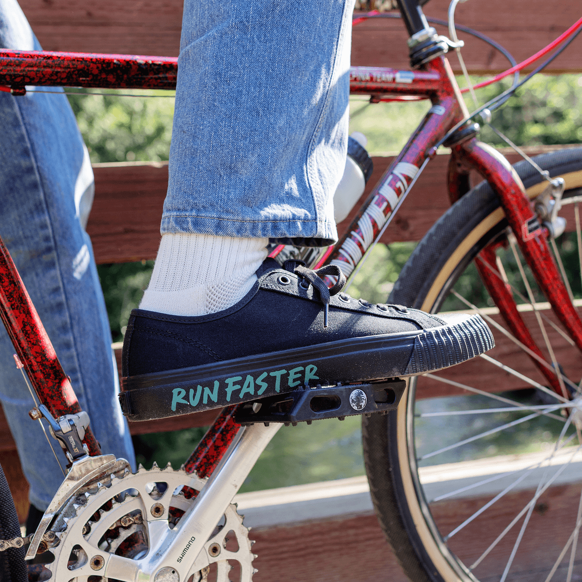 Person wearing a black low-top sneaker with 'Run Faster' text on a bicycle.