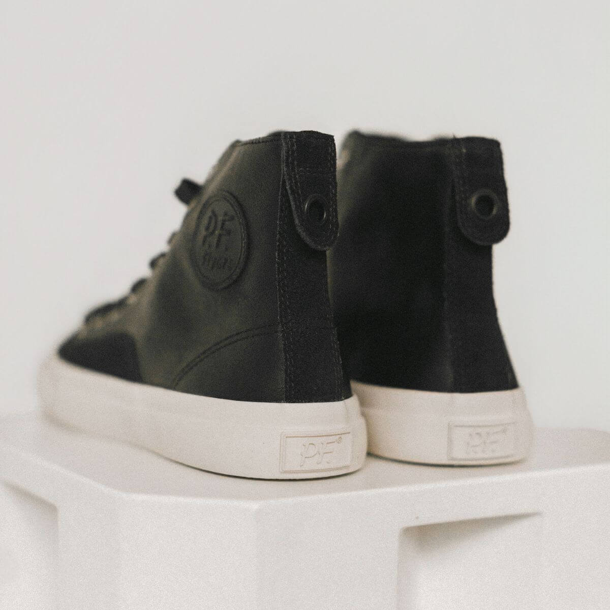Black high-top leather sneakers with white soles on a white surface