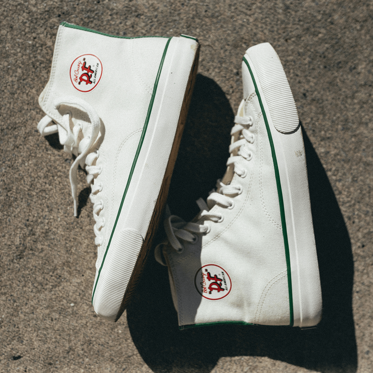White high-top sneakers with green accents on a concrete surface.