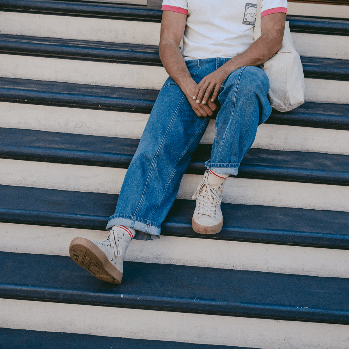Person sitting on a set of outdoor stairs wearing jeans and beige high-top sneakers.
