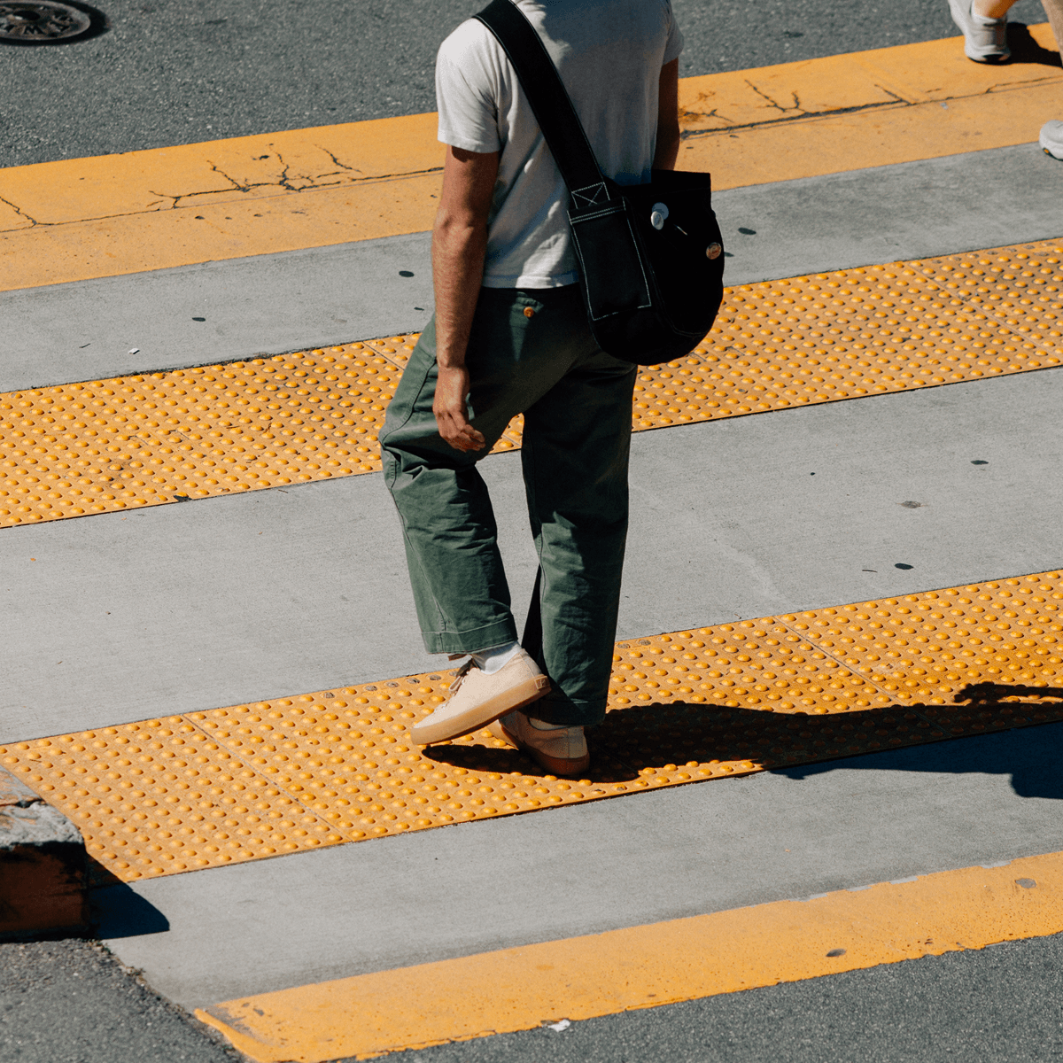 Person walking on a crosswalk wearing beige low-top sneakers.