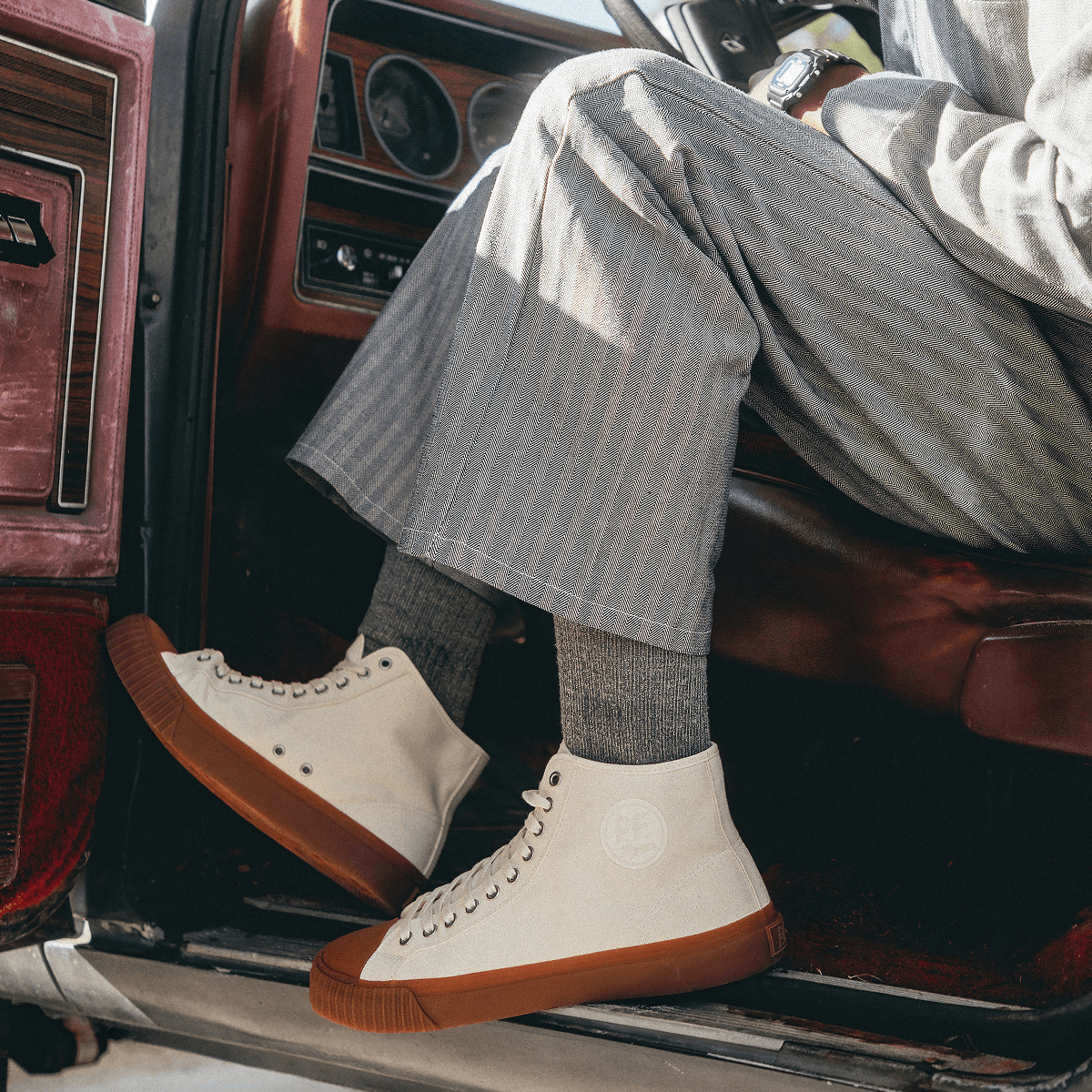 Person wearing white high-top sneakers with brown soles sitting inside a vehicle.