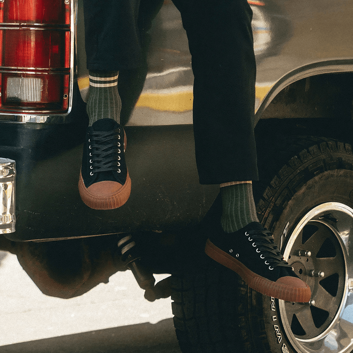 Person sitting on a truck bed wearing black low-top sneakers with brown soles.