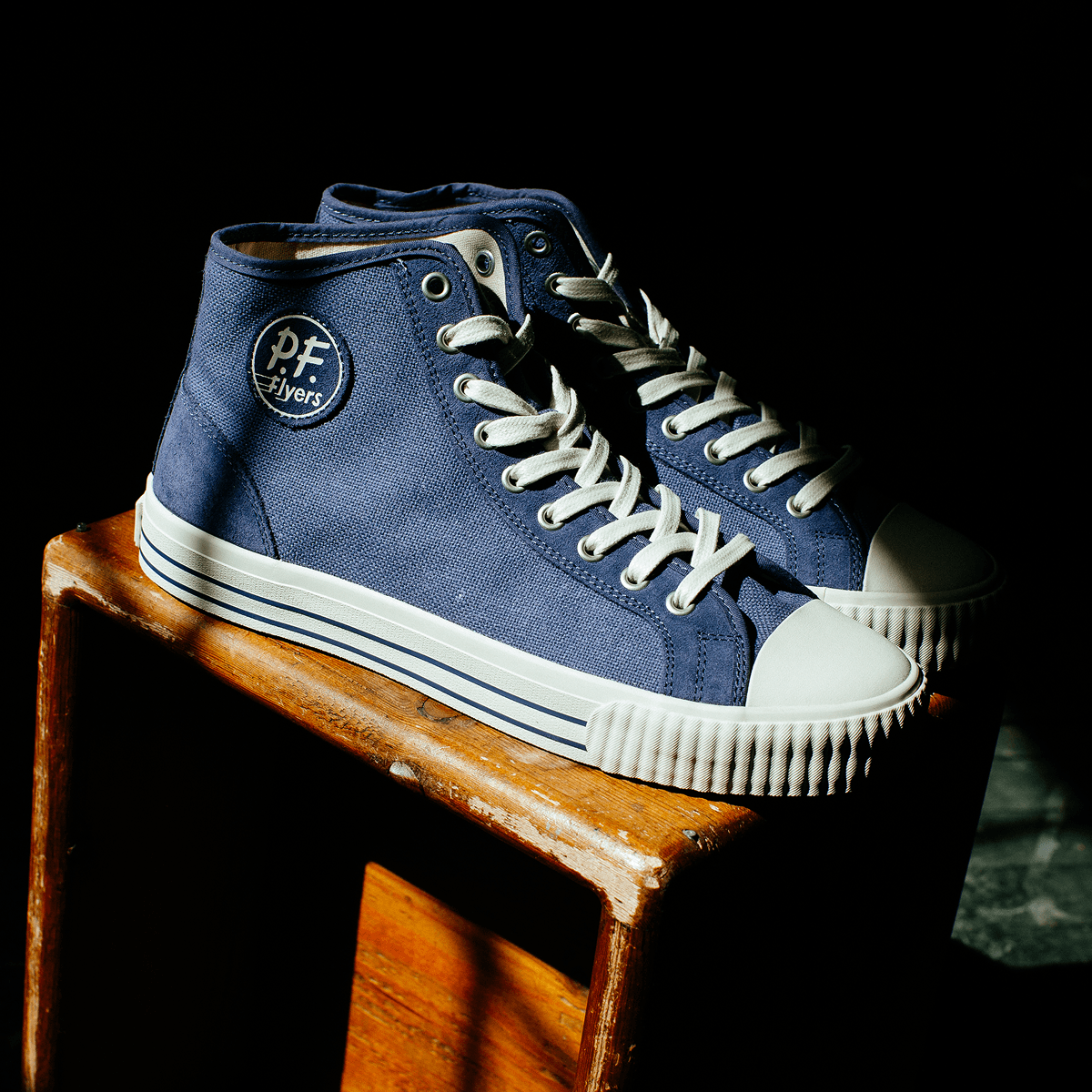 Blue high-top sneakers with white soles on a wooden stool in a dimly lit room.