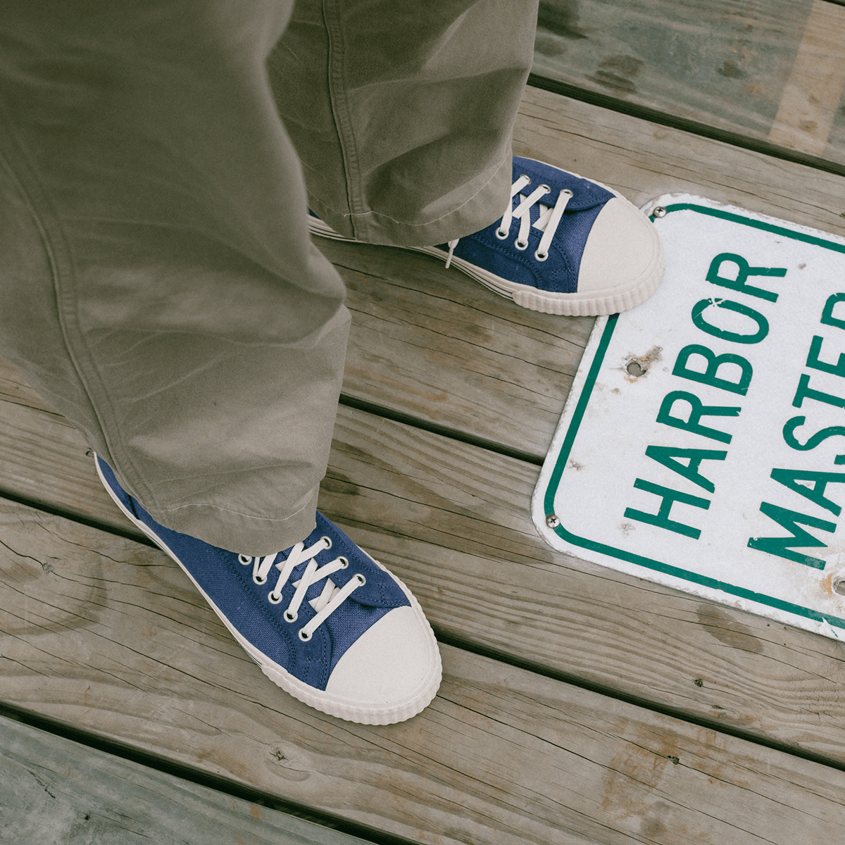Person wearing blue low-top sneakers on a wooden deck with a 'Harbor Master' sign in the background.