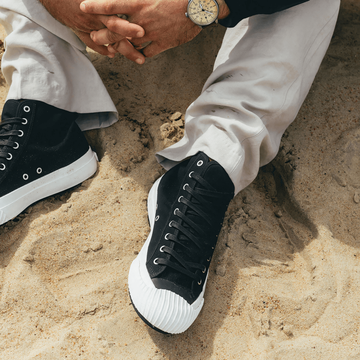 Person wearing black high-top sneakers with white soles on a sand dune.