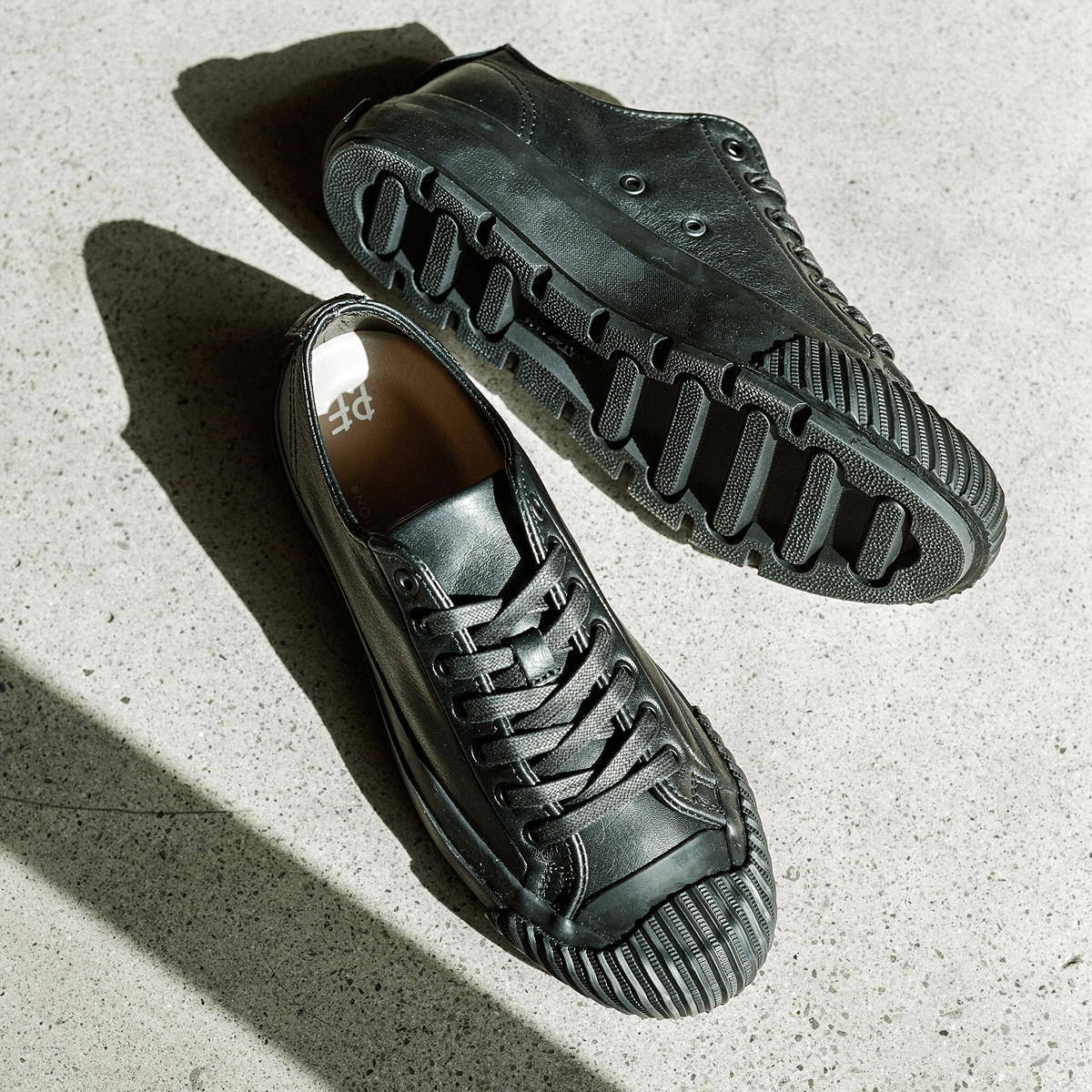 Pair of black leather low-top sneakers on a concrete floor.