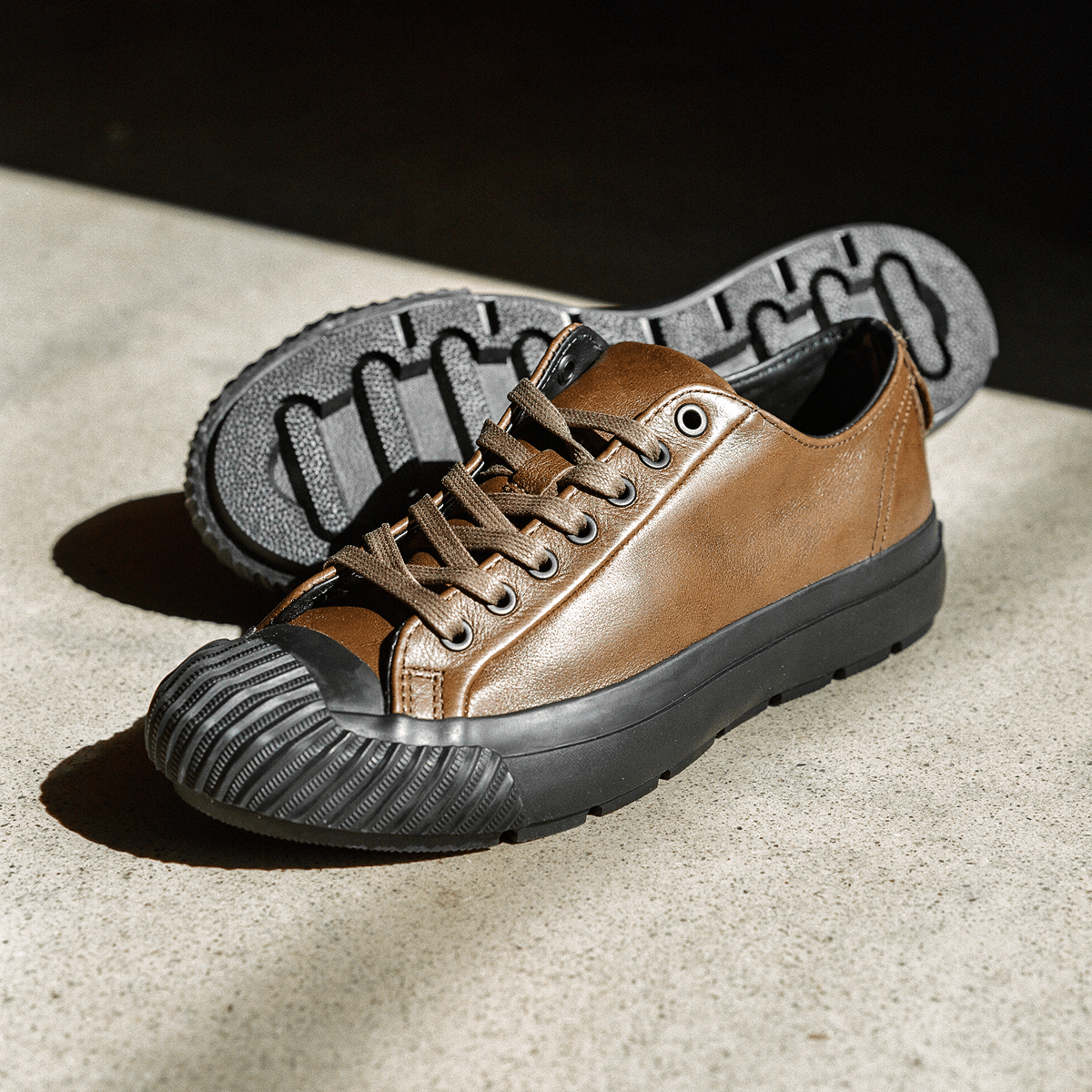 Brown leather low-top sneakers with black soles on a concrete floor.