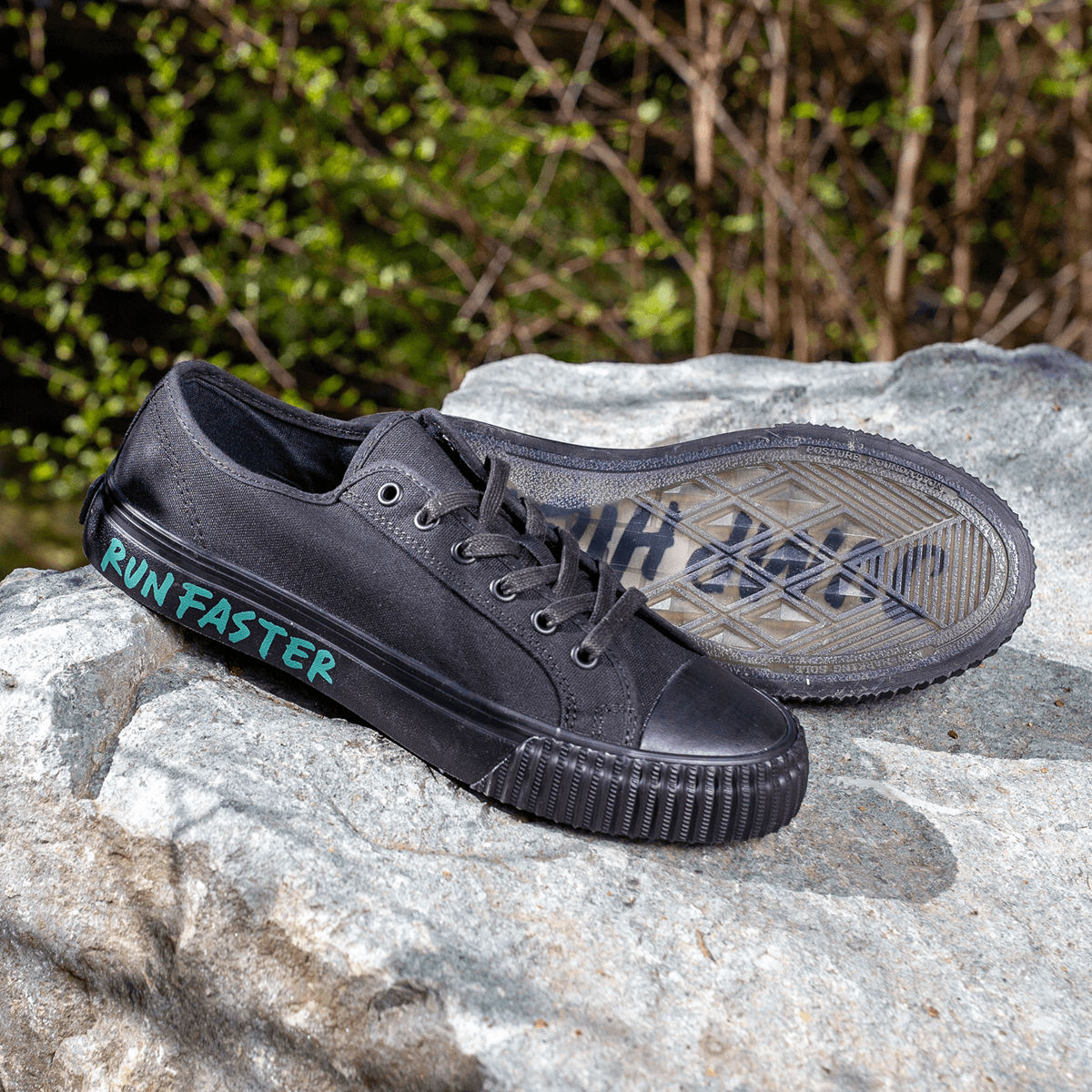 Black low-top sneakers with the phrase 'Run Faster' placed on a rock.