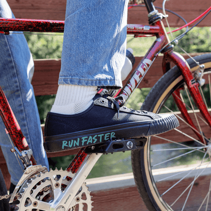 Person wearing a black low-top sneaker with 'Run Faster' text on a bicycle.