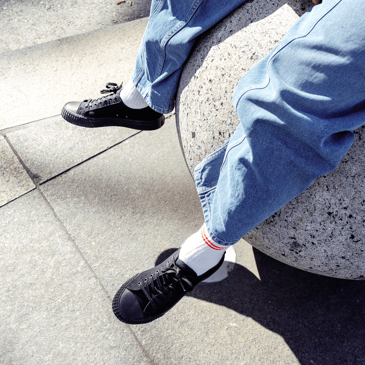 Person sitting on a stone step wearing blue jeans and black low-top shoes.
