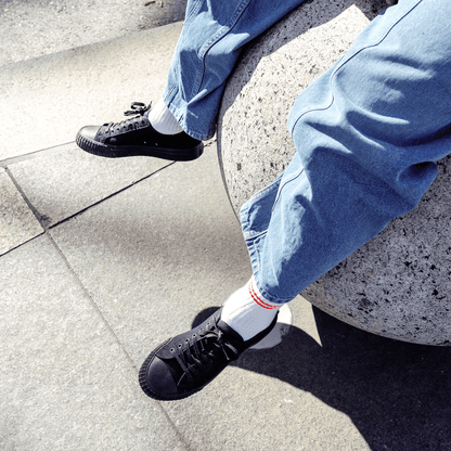 Person sitting on a stone step wearing blue jeans and black low-top shoes.