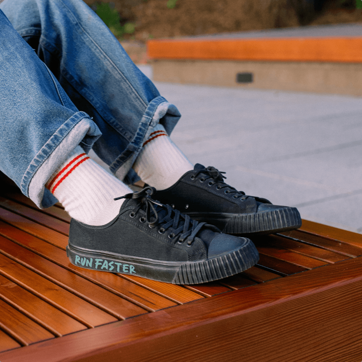 Person wearing black low-top sneakers with 'Run Faster' text, sitting on a wooden bench.