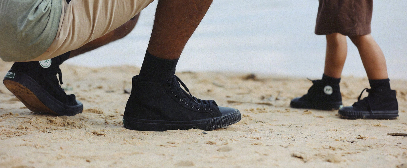 Two people wearing black high-top sneakers on a sandy surface.