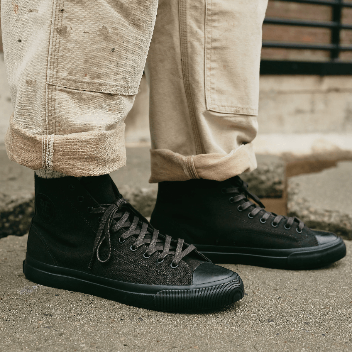 Black high-top sneakers pressed on a cement floor.