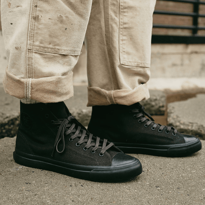 Black high-top sneakers pressed on a cement floor.