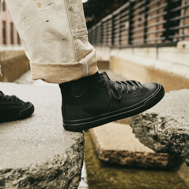 Black high-top sneakers stepping on a stone path.