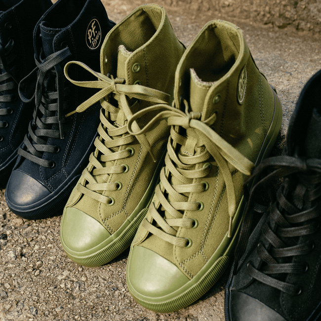 Row of olive green, navy, and black sneakers on a stone step.