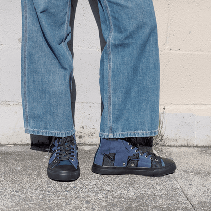 Person wearing blue jeans and black sneakers with blue soles against a light gray wall.
