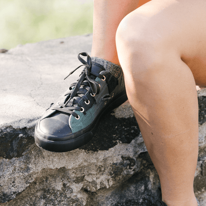Person wearing black high-top sneakers sitting on a stone surface.