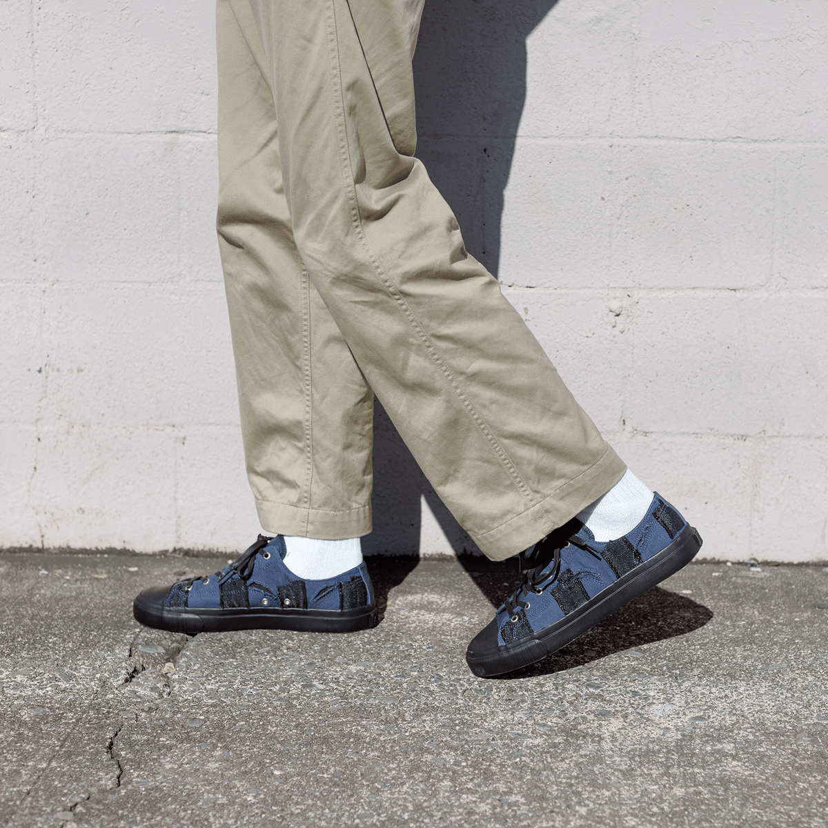 Person wearing beige pants and navy checkered shoes against a gray wall.