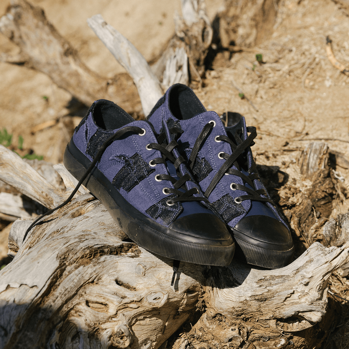 Pair of blue sneakers with black soles on a wooden log