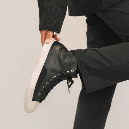 Person wearing black leather high-top sneakers with white soles on a plain background