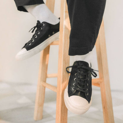 Person wearing black sneakers with white soles on a wooden stool.