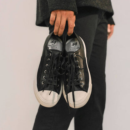 Person holding a pair of black sneakers with white soles against a plain background