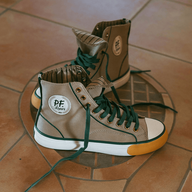 A pair of gray retro high-top sneakers with dark green laces displayed on a tiled floor.