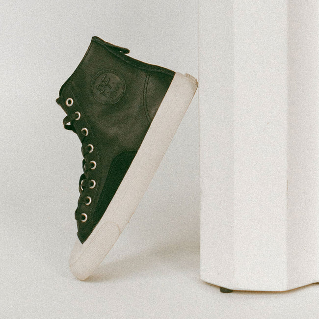 Black high-top sneaker with white sole on a light gray background