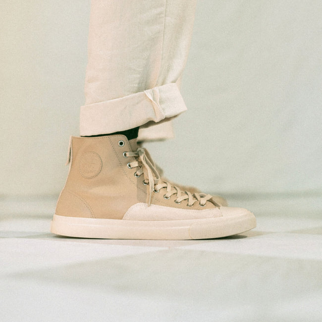 Beige high-top sneakers worn with light-colored pants on a neutral background