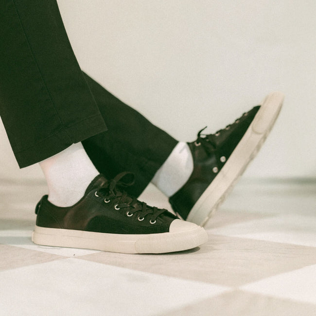 Black sneakers with white soles worn indoors on a checkered floor.
