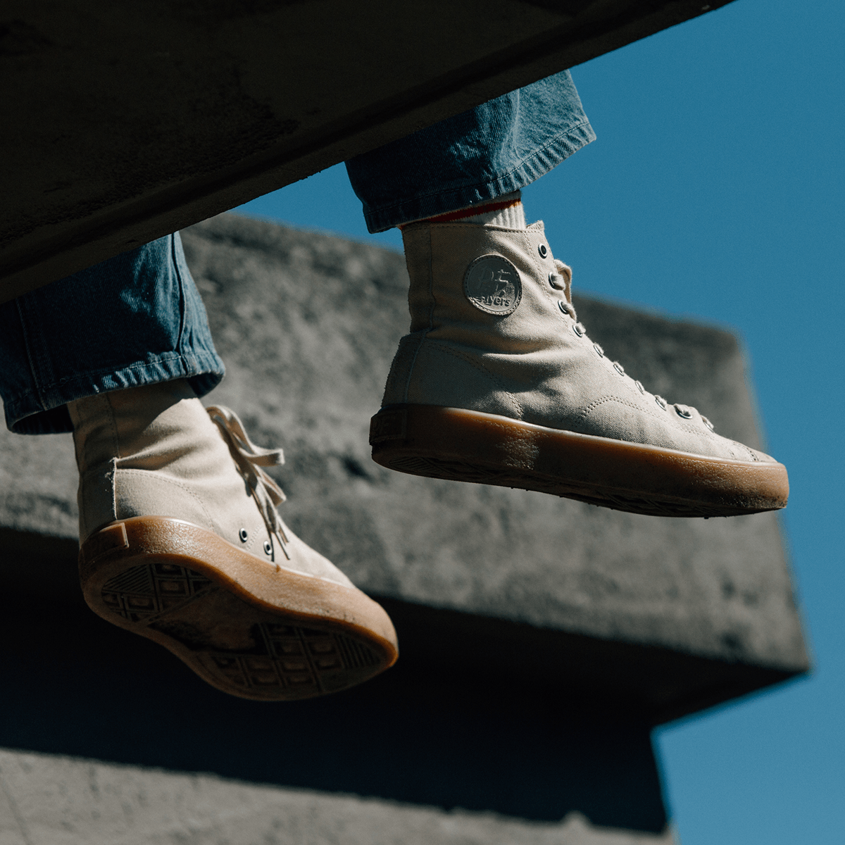 Person wearing beige high-top sneakers with tan soles on a concrete surface against a blue sky.