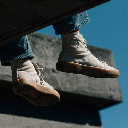 Person wearing beige high-top sneakers with tan soles on a concrete surface against a blue sky.