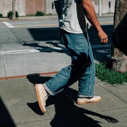 Person walking on a sidewalk wearing blue jeans and beige sneakers.