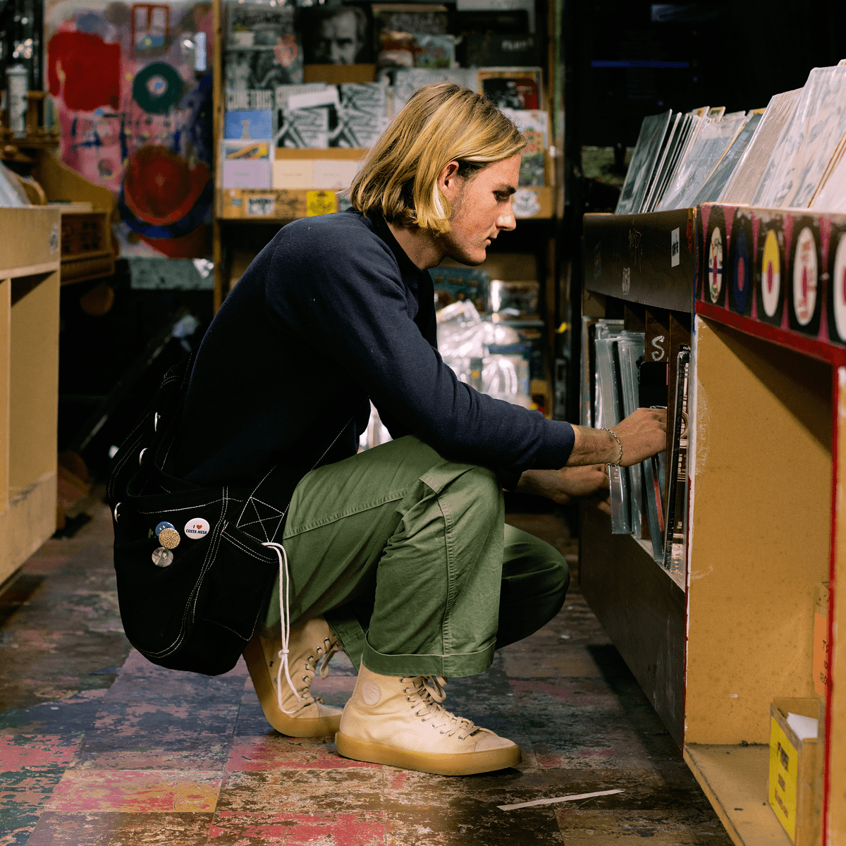 Person browsing records wearing a navy sweater, green pants, and beige high-top sneakers.