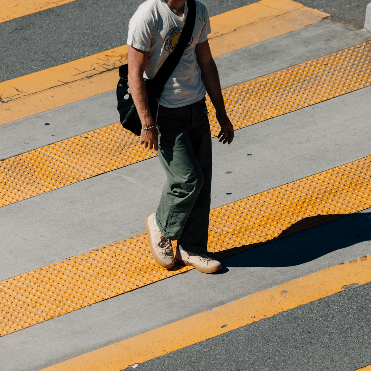 Person walking on a crosswalk wearing beige low-top sneakers.