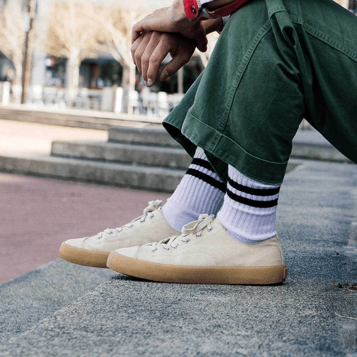 Person sitting on a concrete ledge wearing green pants and beige low-top sneakers in an urban setting.
