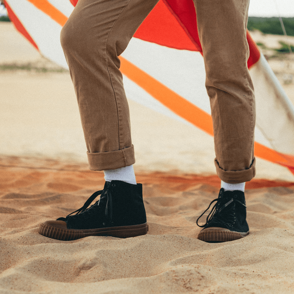 Person standing on sand wearing brown pants and black high-top shoes.