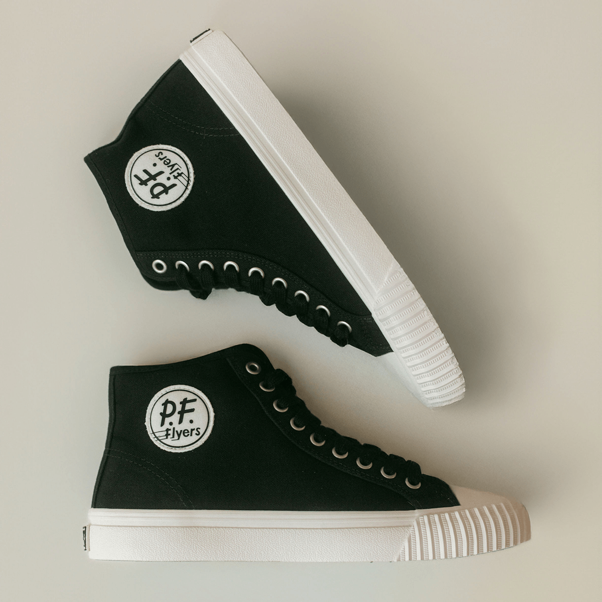Pair of black high-top sneakers with white soles on a light background.