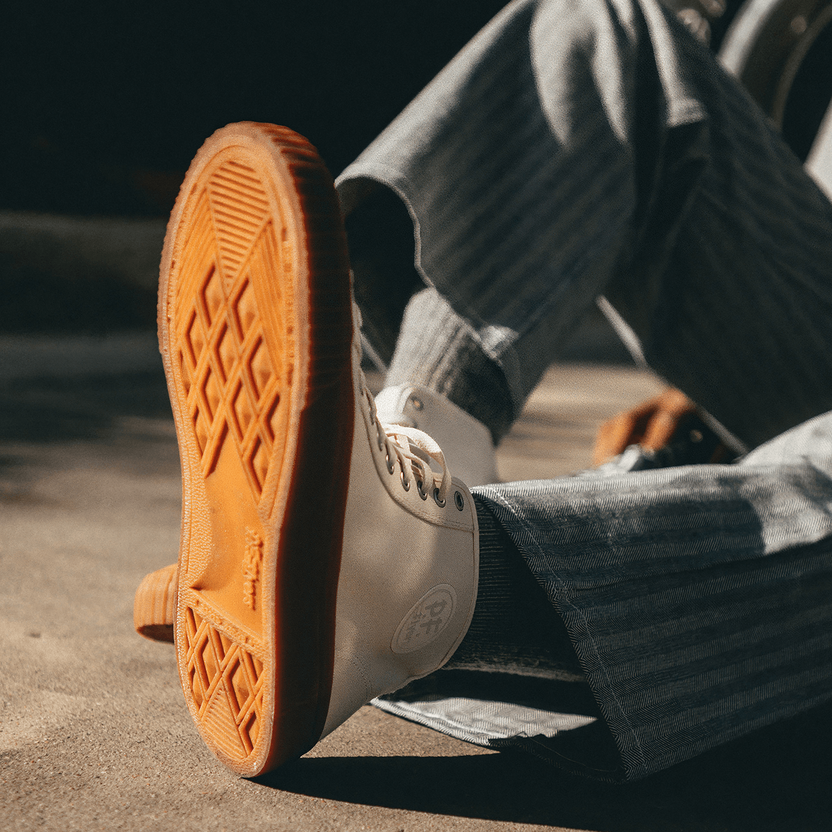 Close-up of a person wearing white sneakers with brown soles on a cement floor.