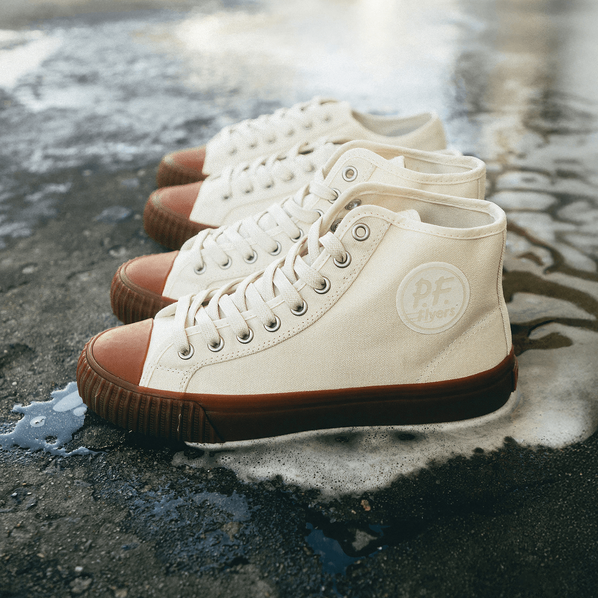 Two pairs of white sneakers with brown soles on a wet pavement.