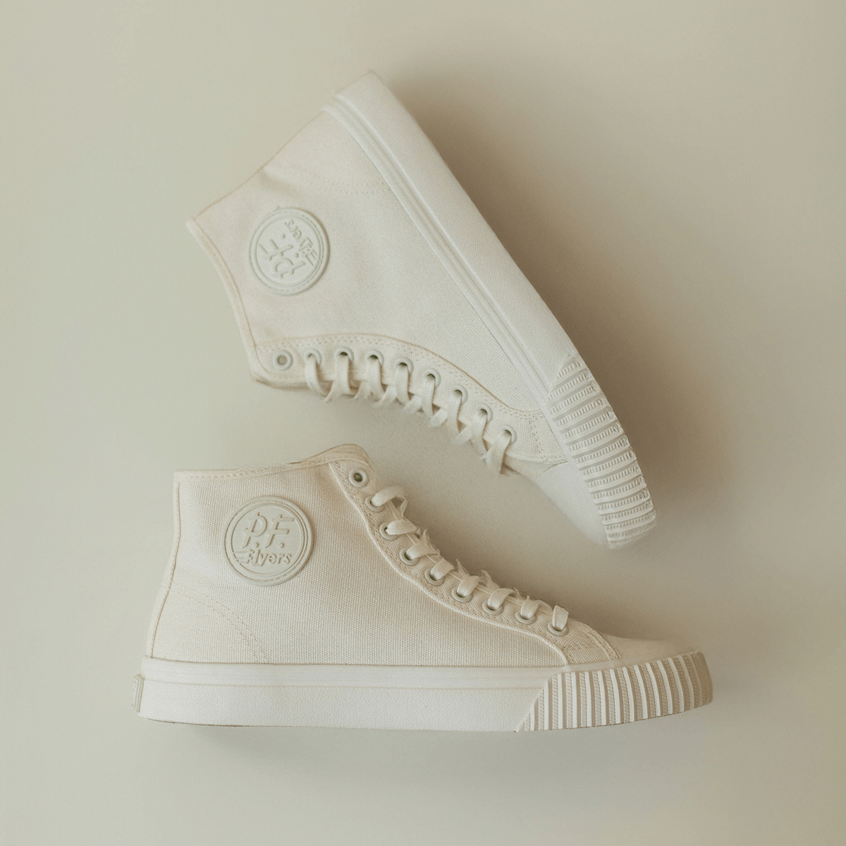 Pair of white high-top sneakers on a beige background.