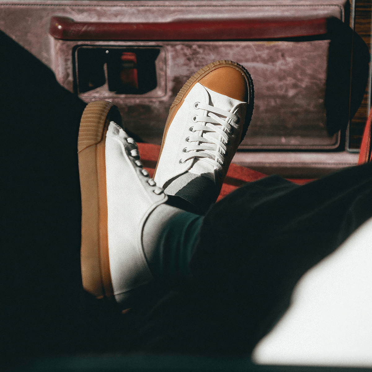 White sneakers with brown soles on a person's feet while sitting inside a vehicle.