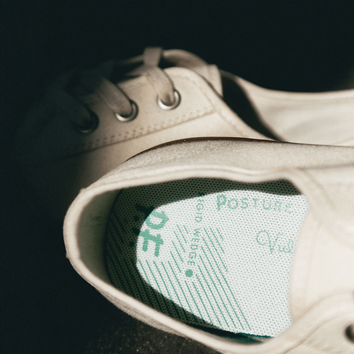 Close-up of a white low-top sneaker with a visible insole label on a dark background.