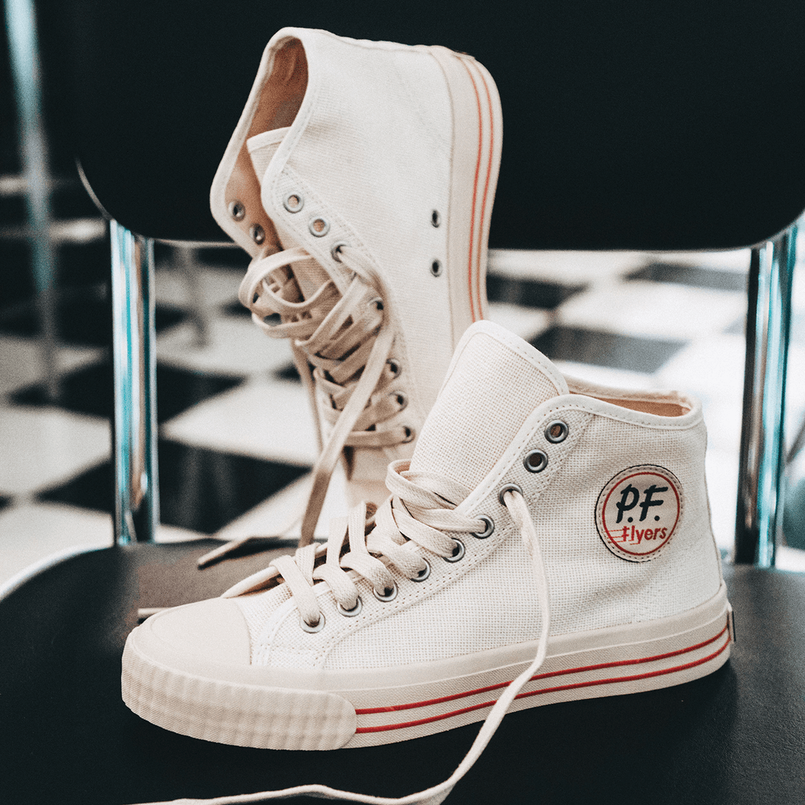 White high-top sneakers with red accents posed on a diner chair.