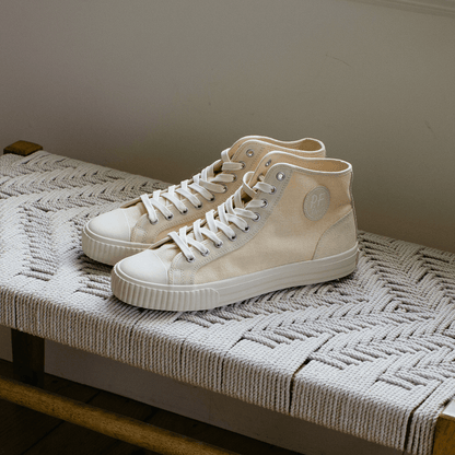 Pair of beige high-top sneakers on a woven bench mat.