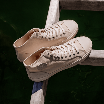 Pair of beige high-top sneakers on a wooden beam over water.